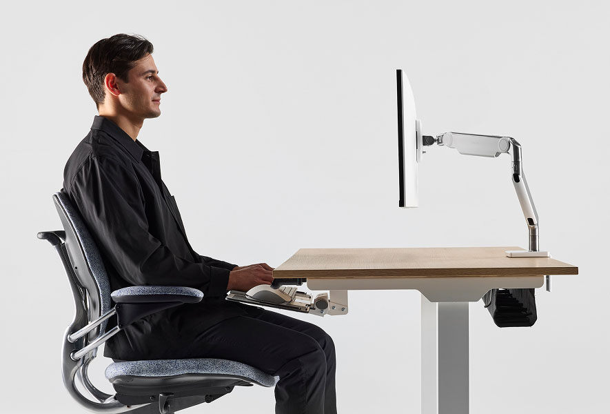 Individual sitting at eFloat Go 2.0 desk, Freedom Task chair, typing on desk-mounted keyboard and M2 Pro